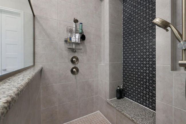 Modern shower with elegant tile work, featuring a mix of neutral and patterned designs. The shower includes a convenient built-in shelf, a sleek showerhead, and a niche for toiletries. | Image 30