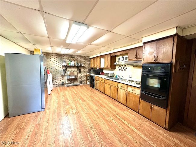 Kitchen with a warming drawer, brick wall, light wood finished floors, appliances with stainless steel finishes, and a paneled ceiling | Image 7