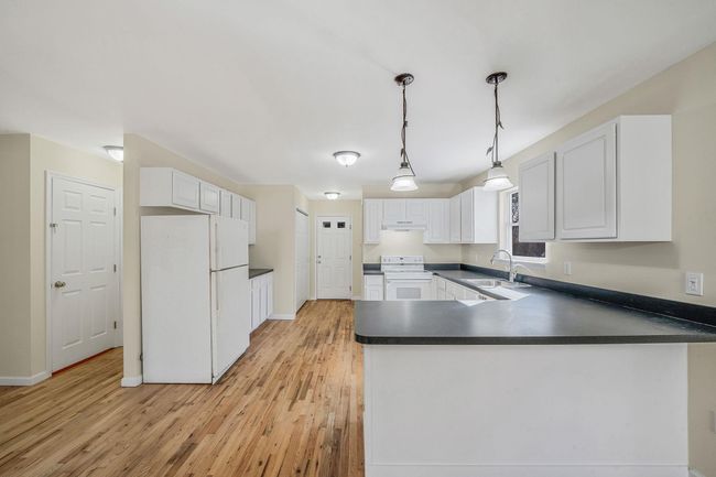 Kitchen with a sink, a peninsula, light wood-style flooring, white appliances, and dark countertops | Image 10