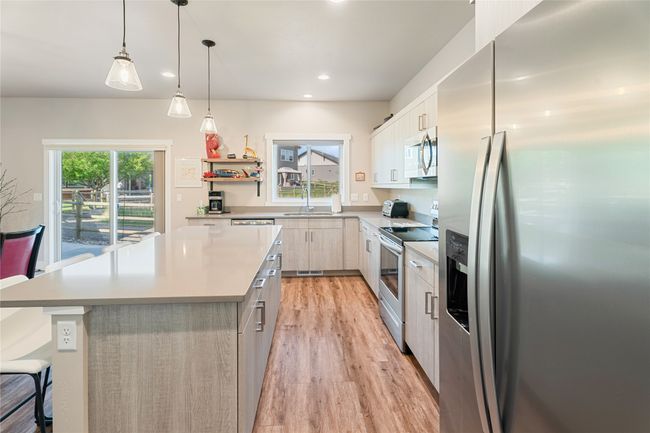 Kitchen with appliances with stainless steel finishes, a kitchen island, light wood-style flooring, modern cabinets, and light countertops | Image 14