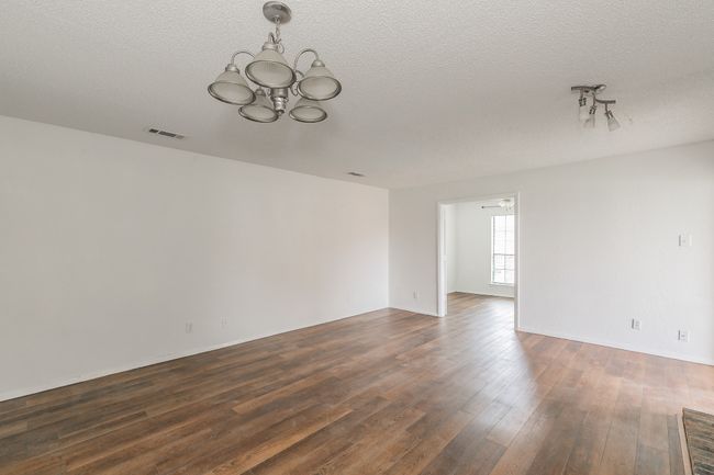 Empty room with a chandelier, dark wood finished floors, and a textured ceiling | Image 6