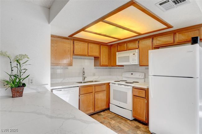 Kitchen featuring a sink, visible vents, decorative backsplash, and white appliances | Image 10