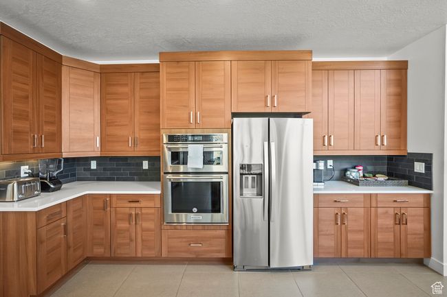 Kitchen featuring appliances with stainless steel finishes, light countertops, backsplash, a textured ceiling, and brown cabinets | Image 13