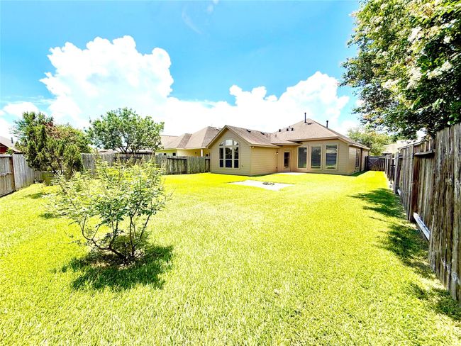 This photo shows a spacious backyard with well-maintained grass and a few trees, enclosed by a wooden fence. The house features large windows and a patio, offering plenty of natural light and outdoor space. | Image 27