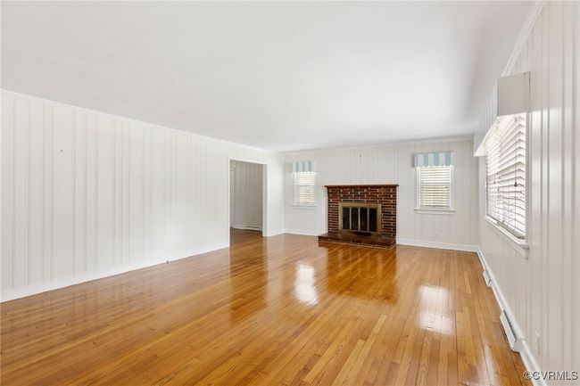 Unfurnished living room with a baseboard heating unit, light wood finished floors, and a brick fireplace | Image 8