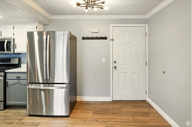 Kitchen with appliances with stainless steel finishes, light wood-type flooring, baseboards, a chandelier, and crown molding | Image 9