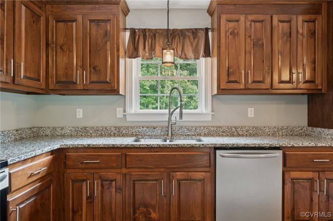 Kitchen with dishwasher, a sink, hanging light fixtures, light stone counters, and brown cabinets | Image 13