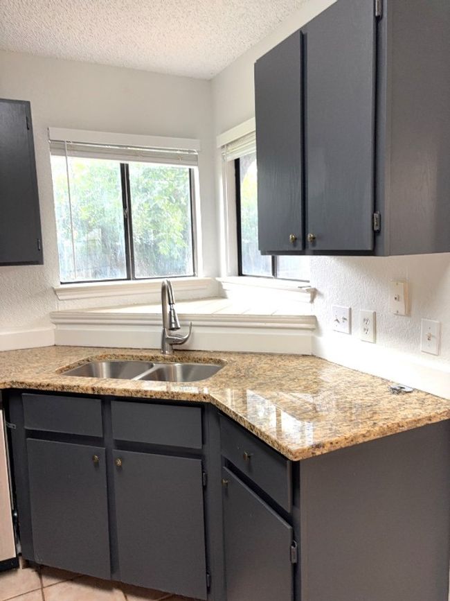 Kitchen with a textured ceiling, gray cabinets, light stone counters, and a textured wall | Image 8