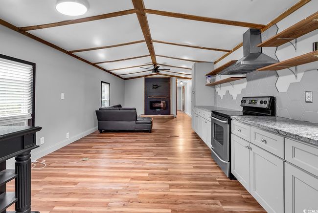 Kitchen with open shelves, electric stove, wall chimney range hood, a sink, and decorative backsplash | Image 6