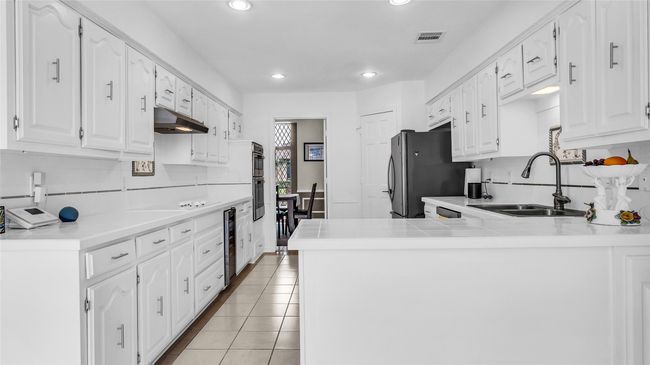 Kitchen featuring under cabinet range hood, wine cooler, recessed lighting, backsplash, and white cabinetry | Image 9