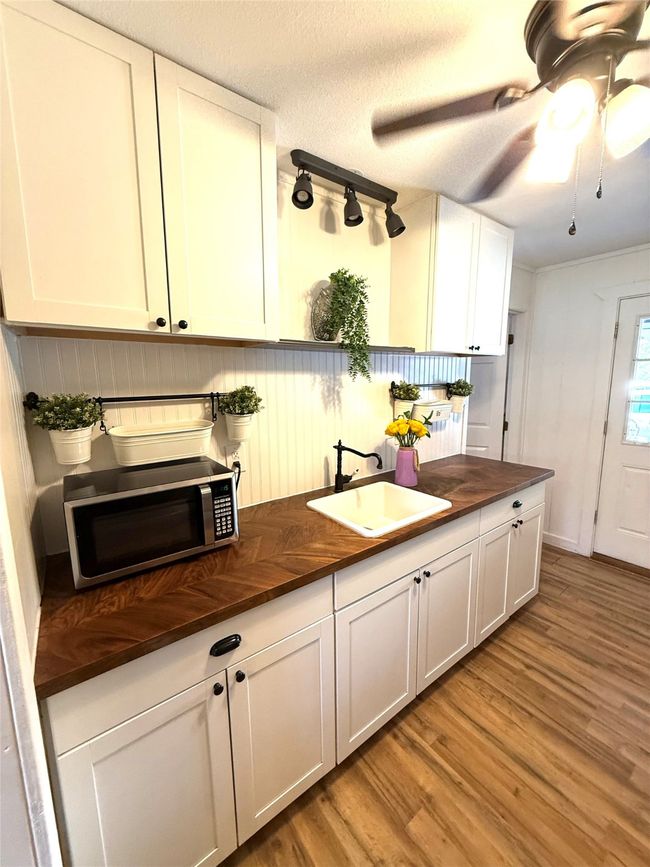Kitchen with light wood-style flooring, white cabinets, wooden counters, stainless steel microwave, and a textured ceiling | Image 7