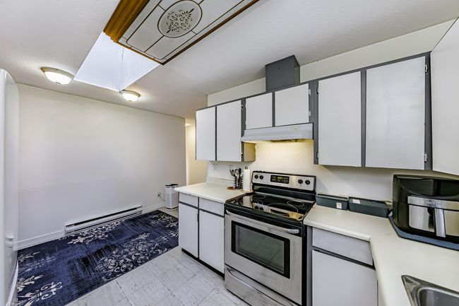 Kitchen featuring under cabinet range hood, a baseboard radiator, light countertops, stainless steel electric range, and a sink | Image 8