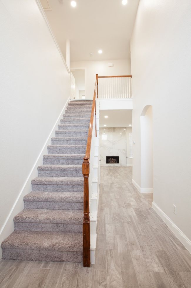 Staircase featuring a fireplace, arched walkways, wood finished floors, recessed lighting, and a high ceiling | Image 4