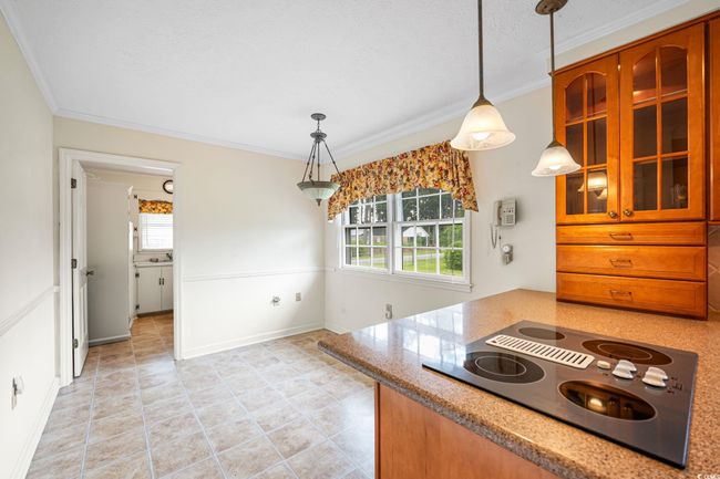 Kitchen with black electric stovetop, ornamental molding, glass insert cabinets, decorative light fixtures, and light stone countertops | Image 9