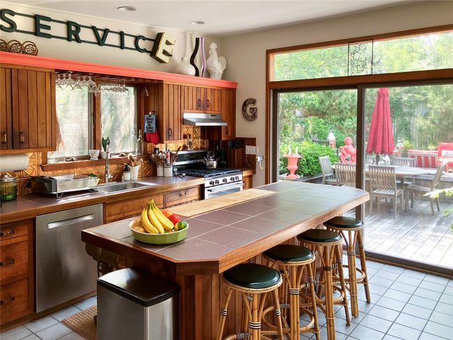 Kitchen with appliances with stainless steel finishes, tile countertops, under cabinet range hood, light tile patterned floors, and brown cabinets | Image 6