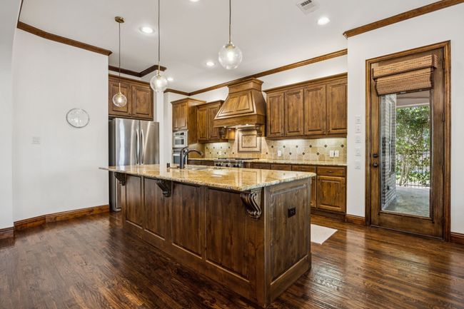 Kitchen featuring premium range hood, ornamental molding, a breakfast bar, dark wood-type flooring, and decorative backsplash | Image 11