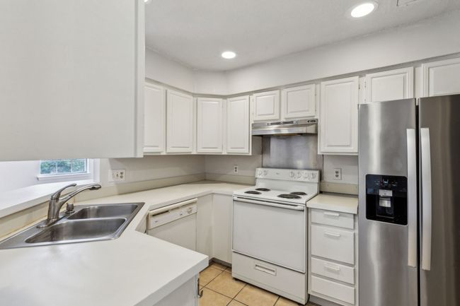Kitchen featuring a sink, light countertops, under cabinet range hood and white cabinetry | Image 16