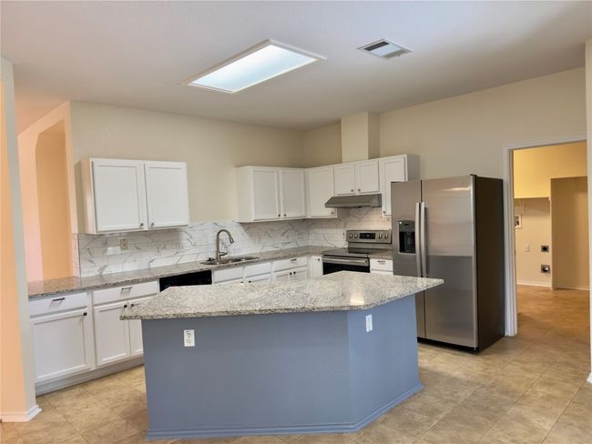 Kitchen featuring appliances with stainless steel finishes, a center island, white cabinetry, backsplash, and light stone countertops | Image 6