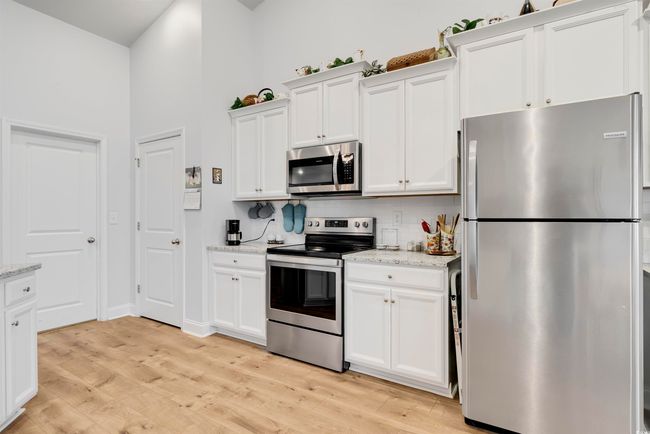 Kitchen with stainless steel appliances, white cabinetry, light wood-type flooring, and light stone counters | Image 4