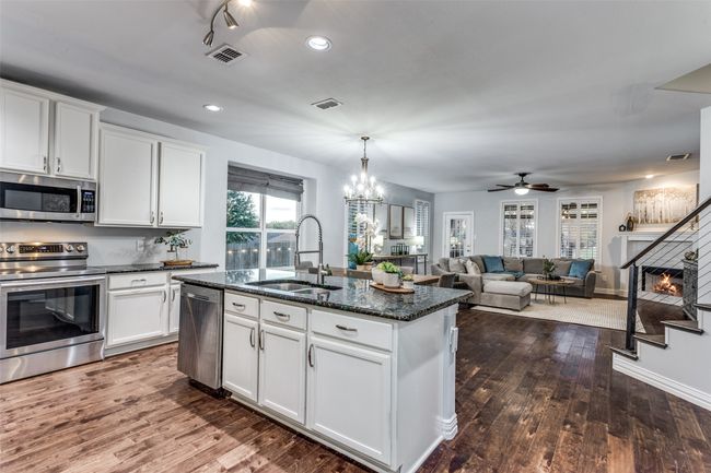 Kitchen featuring appliances with stainless steel finishes, a kitchen island with sink, dark stone counters, dark wood-type flooring, and white cabinets | Image 10