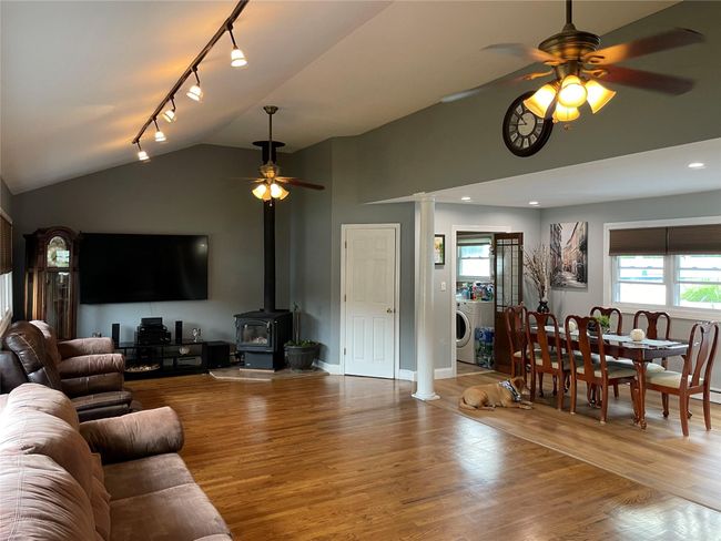 Living room with ceiling fan, wood finished floors, rail lighting, washer / clothes dryer, and a wood stove | Image 12