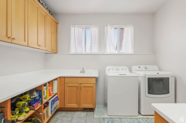 Laundry area featuring light tile patterned floors, washer and dryer, cabinet space, and a sink | Image 10