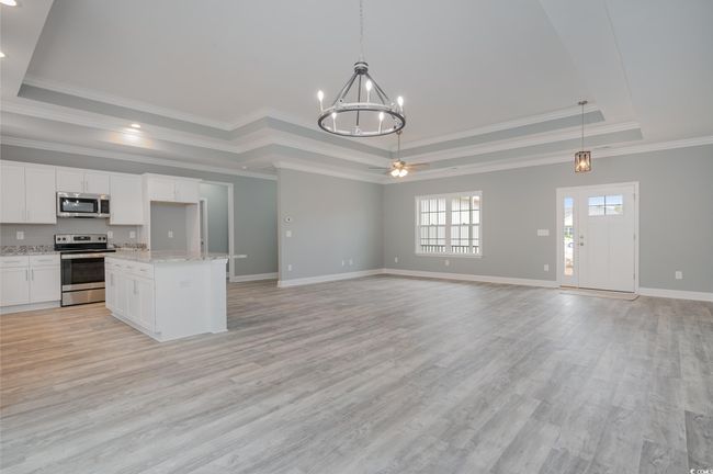 Kitchen with white cabinetry, stainless steel appliances, pendant lighting, light hardwood / wood-style floors, and a tray ceiling | Image 6