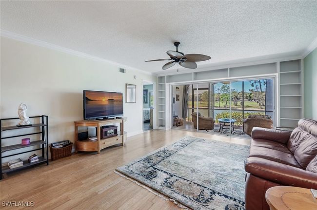 Living area with a textured ceiling, visible vents, ornamental molding, built in shelves, and a ceiling fan | Image 4