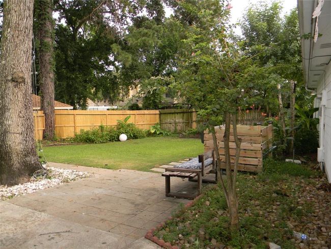 This backyard features a spacious, grassy area with mature trees providing shade. A wooden fence offers privacy, and there's a small patio with stone pavers for outdoor seating. The garden includes a raised planter box, ideal for gardening enthusiasts. | Image 17