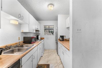 Kitchen with a textured ceiling, white cabinetry, sink, and stainless steel appliances | Image 2