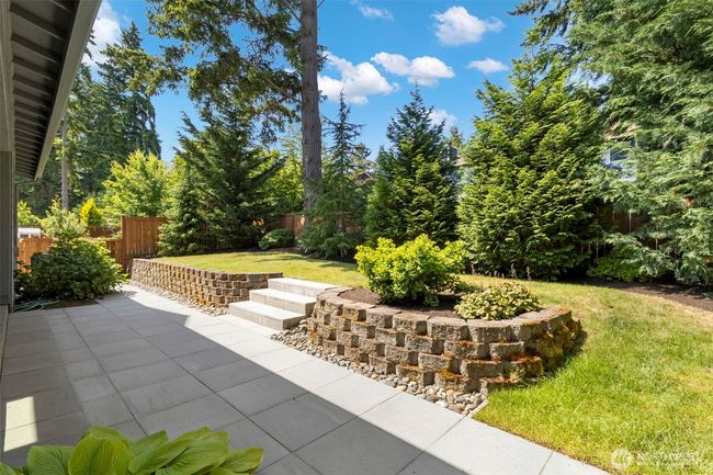 The backyard is a private, sun-dappled oasis bordered by mature evergreens and thoughtfully landscaped with tiered garden beds and stone retaining walls. With a spacious patio and lush lawn, it’s perfect for relaxing, entertaining, or simply enjoying the serenity of nature. | Image 38