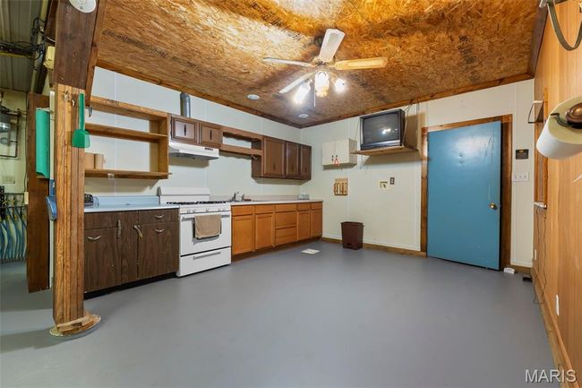 Kitchen featuring white range with gas stovetop, under cabinet range hood, finished concrete floors, and ceiling fan | Image 32