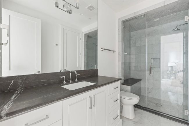 The en suite ground floor bathroom features a stone countertop with furniture-style cabinetry and a frameless glass walk-in shower with bench seating. | Image 41