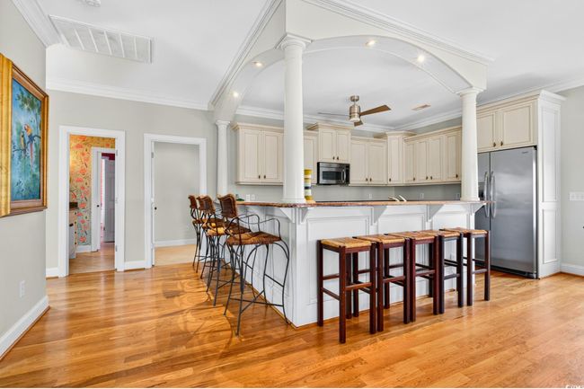 Kitchen featuring appliances with stainless steel finishes, decorative columns, cream cabinetry, a kitchen breakfast bar, and ornamental molding | Image 11