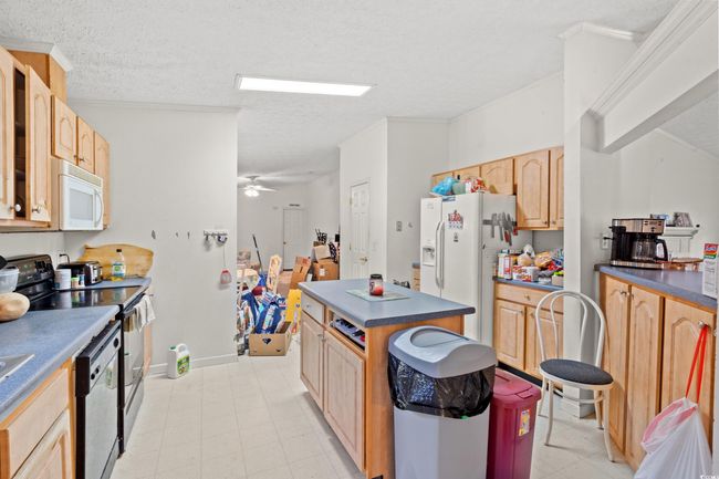 Kitchen with white appliances, dark countertops, light brown cabinets, a textured ceiling, and a center island | Image 9