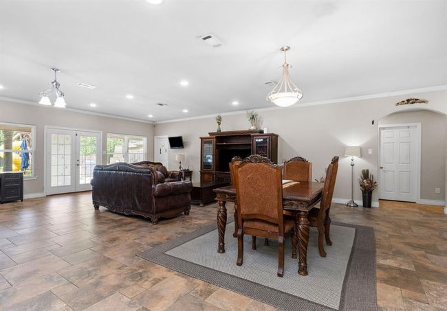 This is a spacious, well-lit combined living and dining area with tiled flooring, elegant light fixtures, and direct access to the backyard through double glass doors. The room features a cozy seating area and a formal dining set, with neutral wall colors offering a canvas for personalization. | Image 42