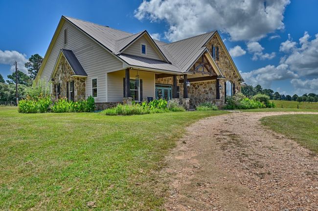 This charming home features a rustic stone and siding exterior with a spacious front porch. It is surrounded by a large yard and set against a backdrop of open fields and trees, ideal for countryside living. | Image 38