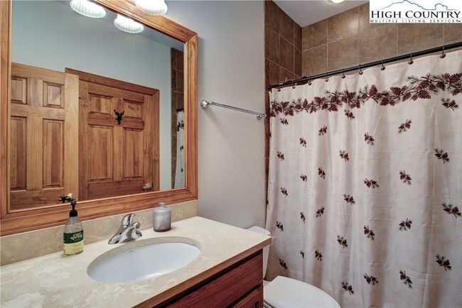 The ensuite guest bath features a ceramic tub/shower with ceramic tile surround. Counter surfaces are stone with undermounted sinks. | Image 38