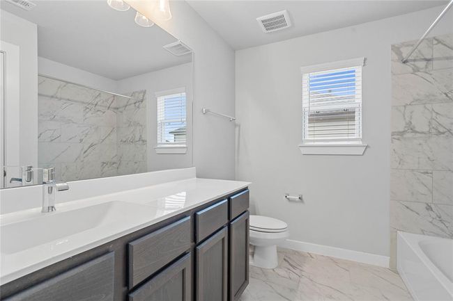 Secondary bath features tile flooring, bath/shower combo with tile surround, stained wood cabinets, beautiful light countertops, mirror, dark, sleek fixtures and modern finishes. | Image 18