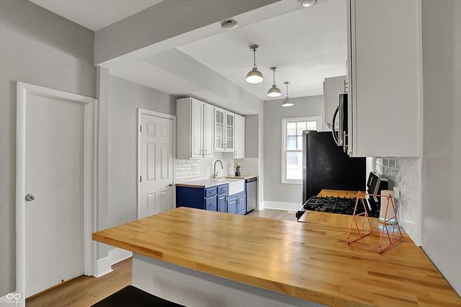 kitchen featuring wood finished floors, white cabinets, blue cabinets, backsplash, and appliances with stainless steel finishes | Image 16