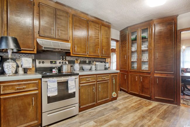 Kitchen featuring stainless steel electric stove, ventilation hood, light countertops, backsplash, and a textured ceiling | Image 10