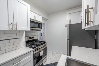 Kitchen with stainless steel appliances, light stone counters, white cabinets, light tile patterned floors, and decorative backsplash | Image 3