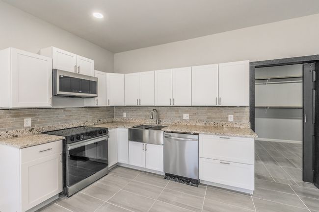 Kitchen featuring decorative backsplash, white cabinets, light stone counters, and appliances with stainless steel finishes | Image 6