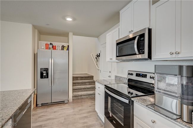 Kitchen with stainless steel appliances, light wood finished floors, white cabinetry, and light stone counters | Image 12