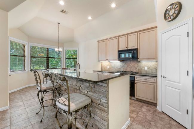 Kitchen with black microwave, tasteful backsplash, lofted ceiling, a kitchen bar, and an island with sink | Image 10