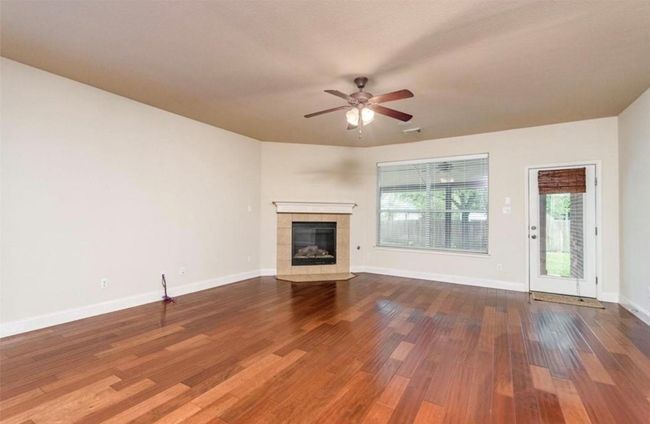 Unfurnished living room with a ceiling fan, a fireplace, wood finished floors, and baseboards | Image 11