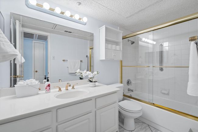 Bathroom featuring combined bath / shower with glass door, vanity, a textured ceiling, toilet, and marble finish floor | Image 28