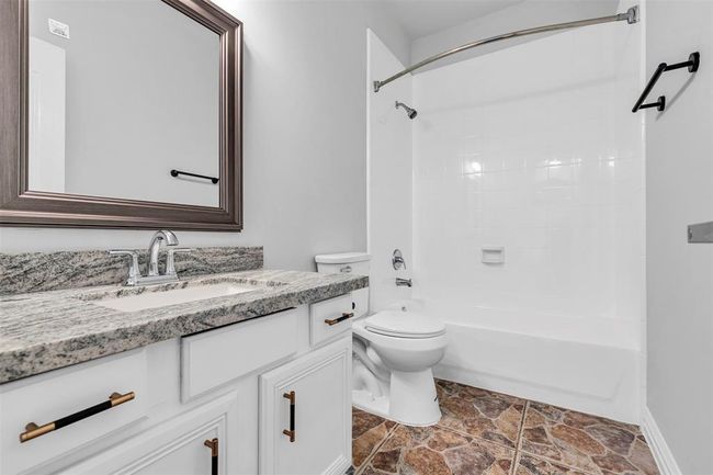 This bathroom features a sleek design with a granite countertop, modern fixtures, and a large framed mirror. It includes a white bathtub with a shower and has stylish tile flooring for a clean, contemporary look. | Image 22