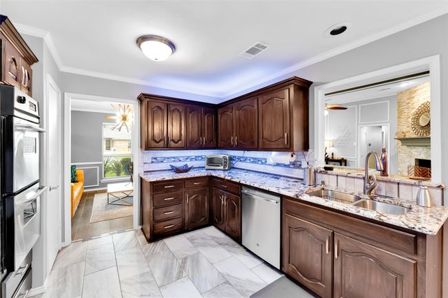 Kitchen featuring appliances with stainless steel finishes, tasteful backsplash, dark brown cabinets, crown molding, and light stone countertops | Image 11