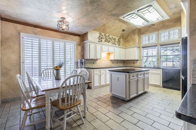 Kitchen with dishwasher, dark countertops, white cabinets, a center island, and a sink | Image 5